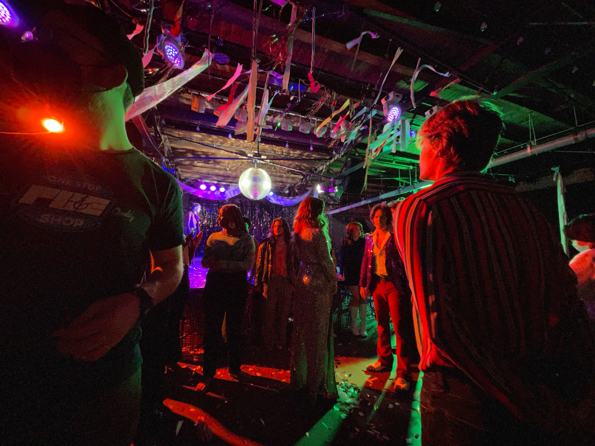 Actors standing in a confetti filled room with a disco ball above.