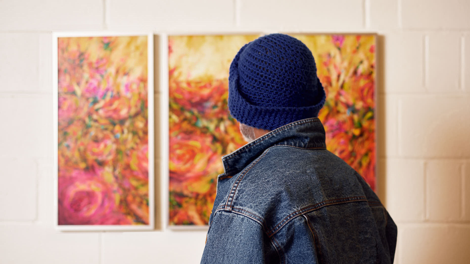 A man looking onward at a pink and red painting of foliage.